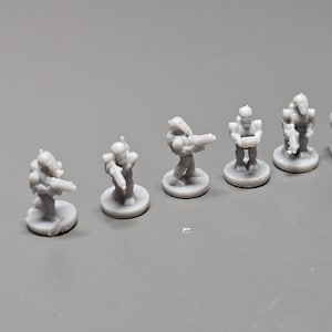 K&ouml;nnte beinhalten: Eine Sammlung kleiner, grauer Miniaturfiguren, die futuristische Soldaten darstellen. Die Figuren stehen auf kreisf&ouml;rmigen Sockeln, einige halten Waffen. Die Miniaturen sind auf einer grauen Oberfl&auml;che angeordnet.