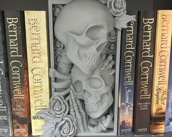 Puede incluir: Un separador de estantería gris con un diseño de calaveras y rosas. Se coloca entre libros de Bernard Cornwell.