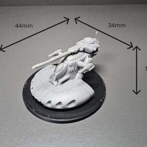 May include: A detailed, unpainted miniature model of a futuristic vehicle, measuring 44mm long, 34mm wide, and 14mm high. The model is mounted on a textured black circular base. The vehicle features intricate details.