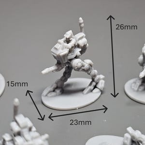 May include: A gray miniature robot figure, 26mm tall and 23mm wide, with a 15mm base. The figure is posed in a dynamic stance, suggesting movement. Several similar figures are visible, indicating a set or collection.