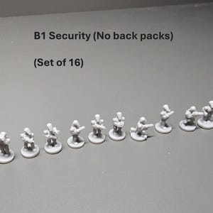 K&ouml;nnte beinhalten: Ein Satz von 16 grauen Miniaturfiguren mit der Aufschrift "B1 Security (No back packs)". Die Figuren befinden sich in verschiedenen Posen, einige stehen und andere knien, und scheinen Waffen zu halten. Die Figuren stehen auf kleinen kreisf&ouml;rmigen Sockeln.