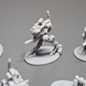 May include: Several gray miniature robot figures are displayed. The robots have a detailed design with articulated limbs and are mounted on circular bases. The figures are likely for tabletop gaming or model building.
