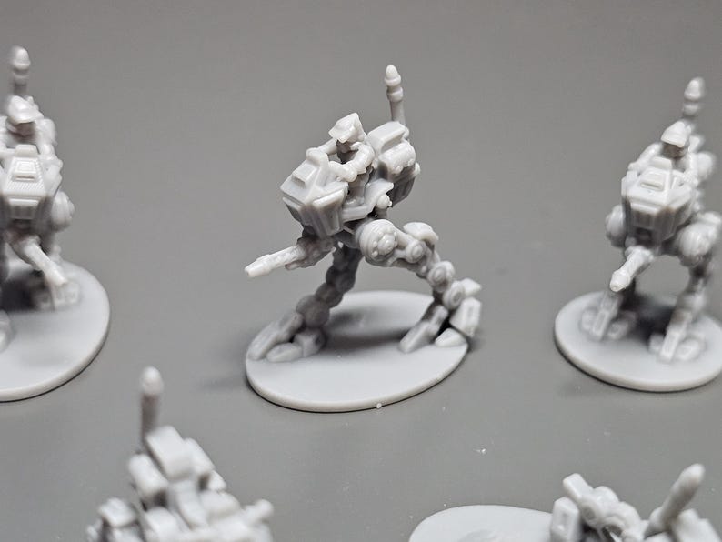 May include: Several gray miniature robot figures are displayed. The robots have a detailed design with articulated limbs and are mounted on circular bases. The figures are likely for tabletop gaming or model building.