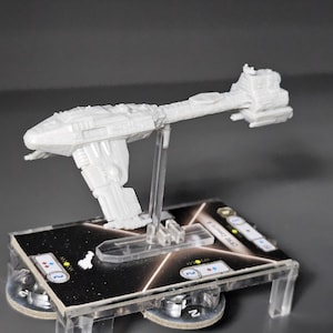 May include: A white plastic model of a spaceship on a clear plastic stand. The spaceship is on a black and white game board with a clear plastic base.