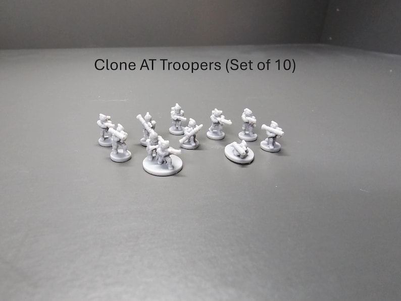 May include: A set of ten grey Clone AT Troopers miniature figures. Each figure is posed with a weapon, standing on a circular base. The text "Clone AT Troopers (Set of 10)" is above the figures.