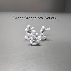 May include: Three small, grey Clone Grenadier figurines are shown, each on a circular base. The text "Clone Grenadiers (Set of 3)" is above the figurines. The figures are in action poses, with one aiming a weapon.