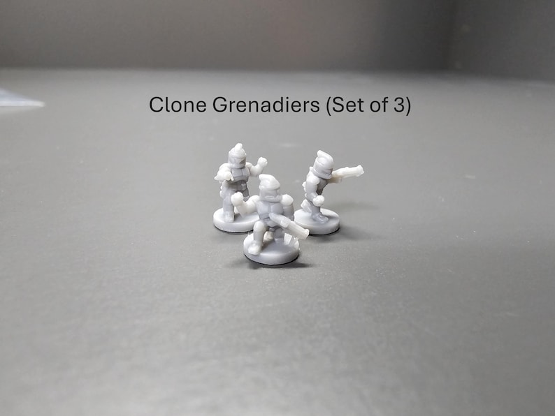 May include: Three small, grey Clone Grenadier figurines are shown, each on a circular base. The text "Clone Grenadiers (Set of 3)" is above the figurines. The figures are in action poses, with one aiming a weapon.