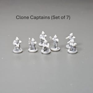 May include: A collection of seven small, grey Clone Captain figurines. Each figurine stands on a circular base and is in a different pose. The text "Clone Captains (Set of 7)" is above the figurines.