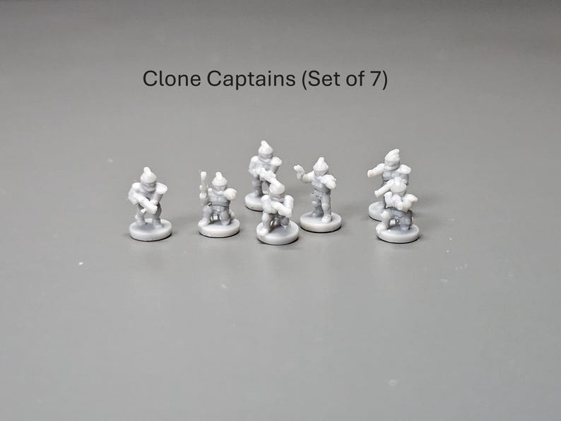 May include: A collection of seven small, grey Clone Captain figurines. Each figurine stands on a circular base and is in a different pose. The text "Clone Captains (Set of 7)" is above the figurines.