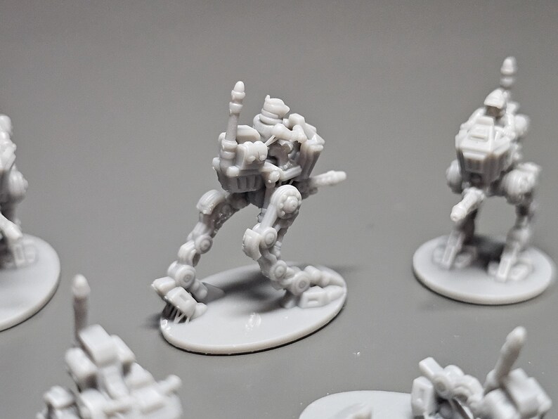 May include: Several small, gray, miniature robot figures are arranged on a gray surface. The robots have articulated limbs and detailed mechanical designs. One robot is in a dynamic pose, with its arm raised. The figures are on oval bases.