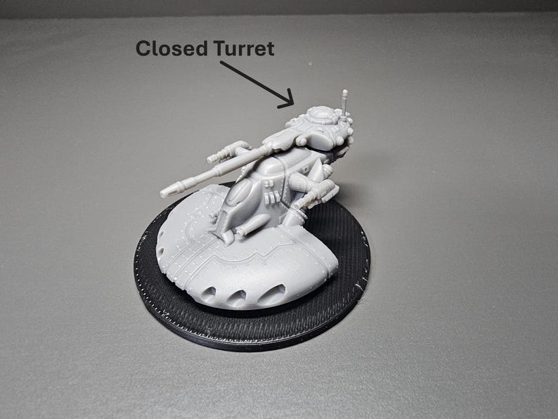 May include: A gray, miniature model of a closed turret vehicle, mounted on a black circular base. The model has detailed weaponry and a futuristic design. The text "Closed Turret" is above the model.
