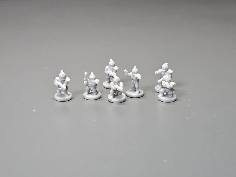 May include: A group of small, grey miniature figurines, likely for tabletop gaming or display. The figures are in different poses, some holding weapons or tools, against a plain grey background. The figurines are approximately 2.5 cm tall.