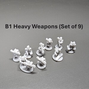 K&ouml;nnte beinhalten: Ein Set aus neun kleinen, grauen B1 Heavy Weapons Miniaturen. Jede Miniatur hat ein einzigartiges Design mit verschiedenen Waffenaufs&auml;tzen. Der Text "B1 Heavy Weapons (Set of 9)" ist oben im Bild zu sehen.