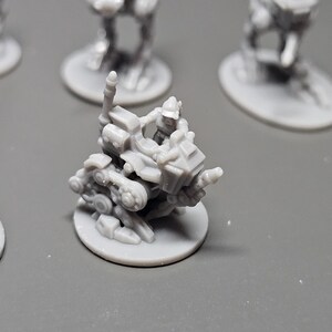 May include: A gray miniature figurine of a futuristic vehicle with a figure in the driver's seat. The vehicle is mounted on a circular base, with other similar figurines in the background. The details of the vehicle are intricate.
