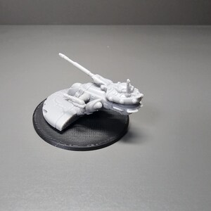 May include: A light gray, 3D-printed model of a futuristic spacecraft, mounted on a black circular base. The spacecraft features intricate details, including a long, angled barrel and various protrusions. The base has a textured surface.