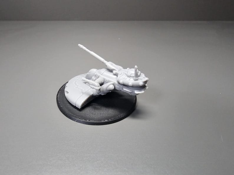 May include: A light gray, 3D-printed model of a futuristic spacecraft, mounted on a black circular base. The spacecraft features intricate details, including a long, angled barrel and various protrusions. The base has a textured surface.