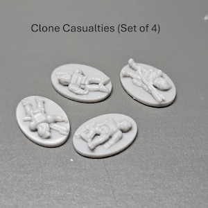 May include: Four grey, oval miniatures depicting fallen soldiers. The text "Clone Casualties (Set of 4)" is above the miniatures. Each miniature shows a detailed figure in a prone position, suggesting a battlefield scene.
