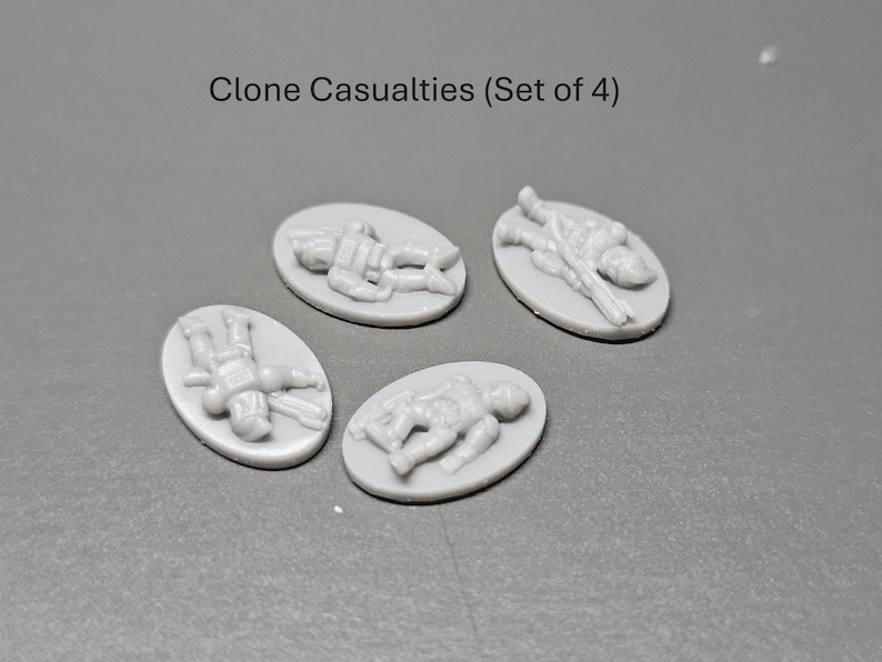 May include: Four grey, oval miniatures depicting fallen soldiers. The text "Clone Casualties (Set of 4)" is above the miniatures. Each miniature shows a detailed figure in a prone position, suggesting a battlefield scene.