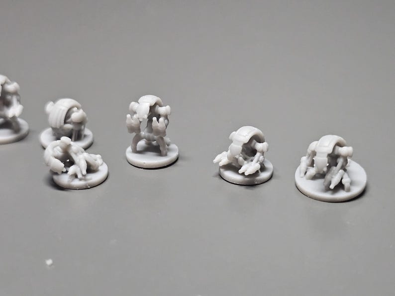 Pode incluir: V&aacute;rias pequenas figuras cinza claro de criaturas semelhantes a insetos. Cada figura est&aacute; em uma pequena base redonda. As criaturas t&ecirc;m v&aacute;rias pernas e um corpo segmentado. As figuras est&atilde;o dispostas em uma superf&iacute;cie cinza.