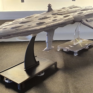 Peut inclure: Un modèle gris détaillé d'un vaisseau spatial sur un socle noir avec des roues. Le vaisseau spatial a un corps long et fin avec un nez pointu et une grande aile plate de chaque côté. Le modèle est sur un socle noir avec des roues.