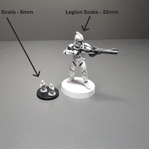 May include: A black and white image shows two miniature figurines and a larger figurine of a soldier holding a weapon. The text in the image indicates the figurines are in Epic Scale (8mm) and Legion Scale (32mm).