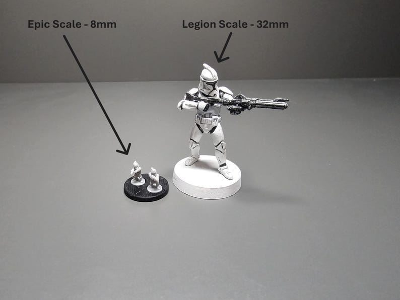 May include: A black and white image shows two miniature figurines and a larger figurine of a soldier holding a weapon. The text in the image indicates the figurines are in Epic Scale (8mm) and Legion Scale (32mm).