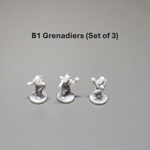 K&ouml;nnte beinhalten: Drei kleine, graue Figuren von B1-Grenadieren werden auf einer grauen Oberfl&auml;che gezeigt. Die Figuren stehen auf kreisf&ouml;rmigen Sockeln. Der Text "B1 Grenadiers (Set of 3)" ist &uuml;ber den Figuren aufgedruckt.