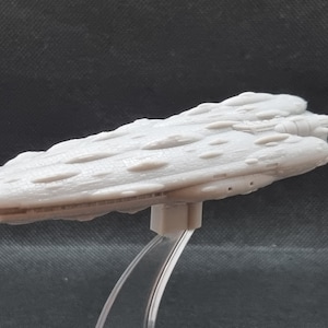 May include: A white, detailed model of a spaceship with a textured surface. The model is on a clear plastic stand.