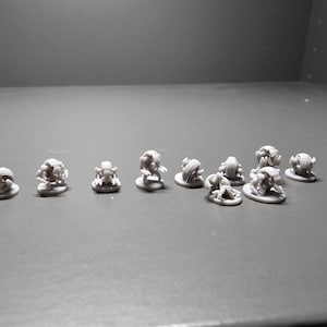 Pode incluir: Uma cole&ccedil;&atilde;o de pequenas figuras cinzentas impressas em 3D. As figuras parecem ser monstros ou criaturas em miniatura, cada uma com um design &uacute;nico. Est&atilde;o dispostas numa superf&iacute;cie cinzenta, adequadas para jogos de mesa ou colecionismo.