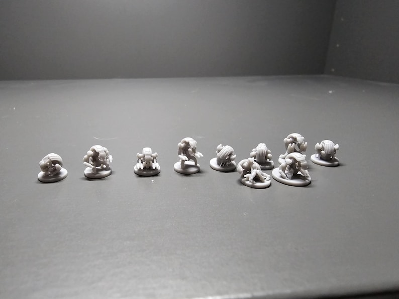 Pode incluir: Uma cole&ccedil;&atilde;o de pequenas figuras cinzentas impressas em 3D. As figuras parecem ser monstros ou criaturas em miniatura, cada uma com um design &uacute;nico. Est&atilde;o dispostas numa superf&iacute;cie cinzenta, adequadas para jogos de mesa ou colecionismo.