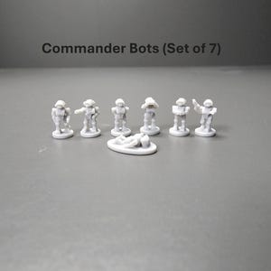 K&ouml;nnte beinhalten: Ein Set aus sieben kleinen, grauen Commander Bots-Figuren. Jeder Bot befindet sich in einer anderen Pose, einer liegt auf einer kleinen, ovalen Basis. Der Text "Commander Bots (Set of 7)" befindet sich &uuml;ber den Figuren.