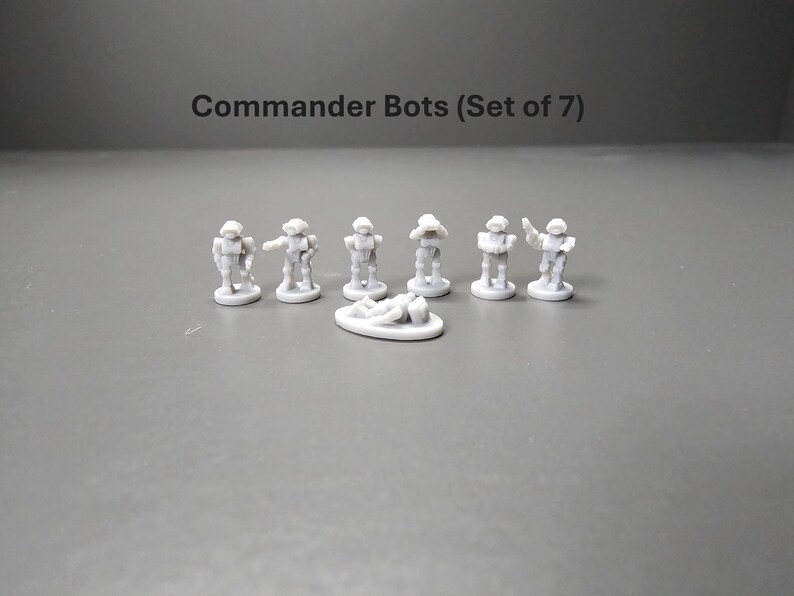 K&ouml;nnte beinhalten: Ein Set aus sieben kleinen, grauen Commander Bots-Figuren. Jeder Bot befindet sich in einer anderen Pose, einer liegt auf einer kleinen, ovalen Basis. Der Text "Commander Bots (Set of 7)" befindet sich &uuml;ber den Figuren.