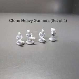May include: Four small, grey Clone Heavy Gunners figurines. Each figure is posed with a weapon, standing on a small, round base. The text "Clone Heavy Gunners (Set of 4)" is above the figurines.