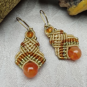 May include: A pair of handmade earrings with a macrame design in beige and brown with orange gemstone accents.