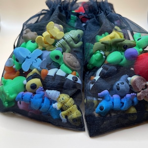 K&ouml;nnte beinhalten: Zwei schwarze Netztaschen gef&uuml;llt mit einer Vielzahl von bunten kleinen Gummispielzeug. Die Spielzeuge sind in Form von Tieren, Insekten und anderen Objekten.