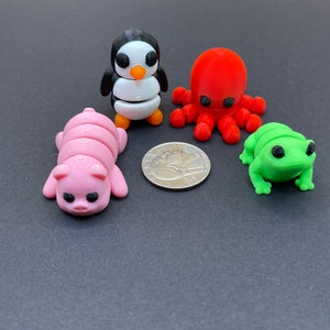 K&ouml;nnte beinhalten: Ein Set aus vier kleinen, bunten, 3D-gedruckten Tierfiguren: ein rosa Schwein, ein schwarz-wei&szlig;er Pinguin, ein roter Tintenfisch und ein gr&uuml;ner Frosch. Die Figuren sind etwa so gro&szlig; wie eine US-amerikanische 25-Cent-M&uuml;nze.