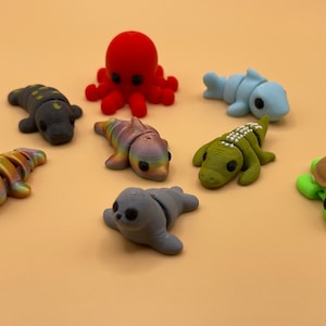 K&ouml;nnte beinhalten: Ein Set aus acht farbenfrohen, handbemalten Meereslebewesen-Figuren. Die Figuren umfassen einen Oktopus, einen Delfin, einen Hai, eine Schildkr&ouml;te, eine Robbe, ein Eidechse und zwei Fische. Die Figuren sind aus einem glatten, strapazierf&auml;higen Material gefertigt und perfekt, um jedem Wohndekor einen Hauch von Verspieltheit zu verleihen.