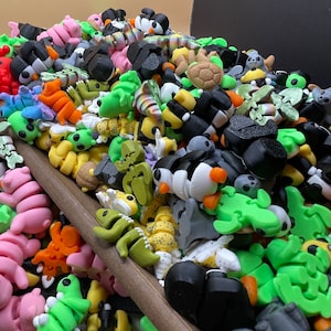 K&ouml;nnte beinhalten: Eine gro&szlig;e Sammlung kleiner, bunter Plastikfiguren. Die Figuren sind in Form von Tieren, Insekten und anderen Kreaturen gestaltet. Sie sind auf einer Holzoberfl&auml;che zu einem Haufen zusammengestellt.