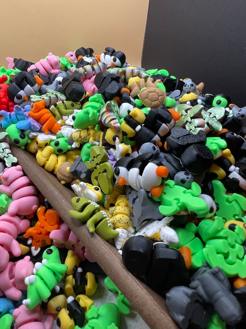 K&ouml;nnte beinhalten: Eine gro&szlig;e Sammlung kleiner, bunter Plastikfiguren. Die Figuren sind in Form von Tieren, Insekten und anderen Kreaturen gestaltet. Sie sind auf einer Holzoberfl&auml;che zu einem Haufen zusammengestellt.