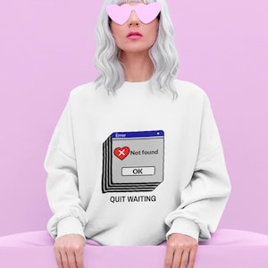 Könnte beinhalten: Ein weißes Langarm-Sweatshirt mit einer Grafik eines gestapelten Computer-Fehlerfensters, einem roten Herz-Symbol, dem Text "Error", "Not found", "OK" und dem Schriftzug "QUIT WAITING" in schwarzer Farbe darunter.