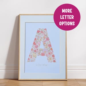May include: A framed print with a light blue background featuring a large letter A made of a floral pattern in pink, red, and yellow. The text "A is for Alba" is printed below the letter.