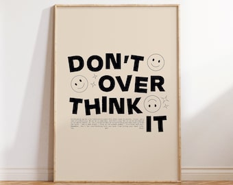 May include: A beige poster with a black and white graphic design that says "Don't Overthink It" with smiley faces and stars. The poster is framed in a light wood frame.