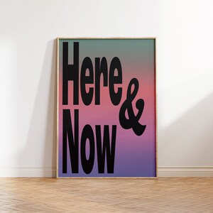 May include: A framed poster with a gradient background in shades of blue, pink, and purple. The text "Here & Now" is printed in black bold letters.