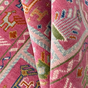 Puede incluir: Primer plano de una alfombra rosa con un patrón geométrico en tonos de azul, verde y naranja. La alfombra está hecha de lana y tiene una textura suave y mullida.