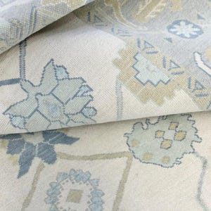 May include: A white rug with a blue and beige floral pattern. The rug has a soft, textured surface and a subtle sheen.