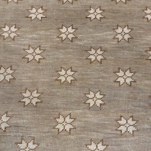Op de afbeelding: Een beige kleed met een herhalend patroon van witte stervormige ontwerpen.