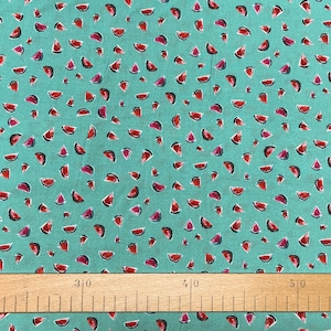Könnte beinhalten: Türkiser Stoff mit einem sich wiederholenden Muster aus roten Wassermelonenstücken. Der Stoff wird mit einem Lineal aus Holz gemessen, das in Zoll eingeteilt ist.