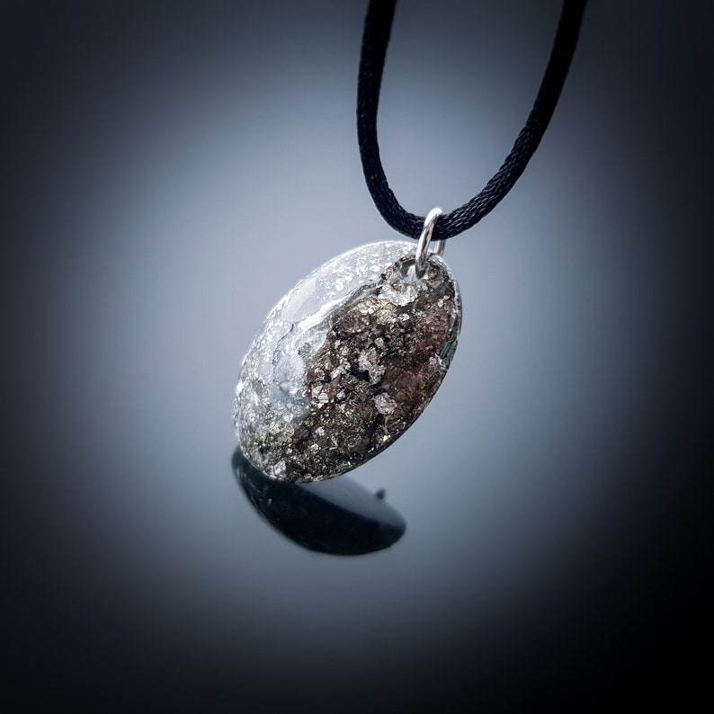 May include: A silver oval pendant necklace with a black cord. The pendant is filled with a clear resin and contains small pieces of gold glitter.