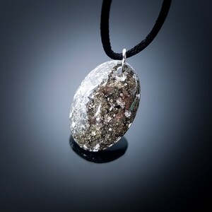 May include: A silver oval pendant necklace with a black cord. The pendant is filled with a mixture of silver and black glitter.