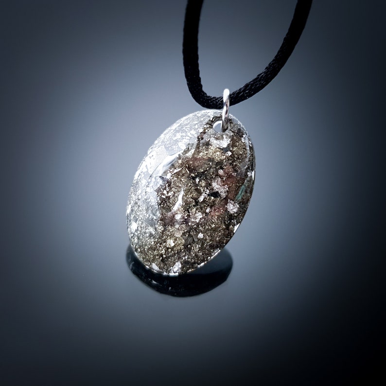 May include: A silver oval pendant necklace with a black cord. The pendant is filled with a mixture of silver and black glitter.